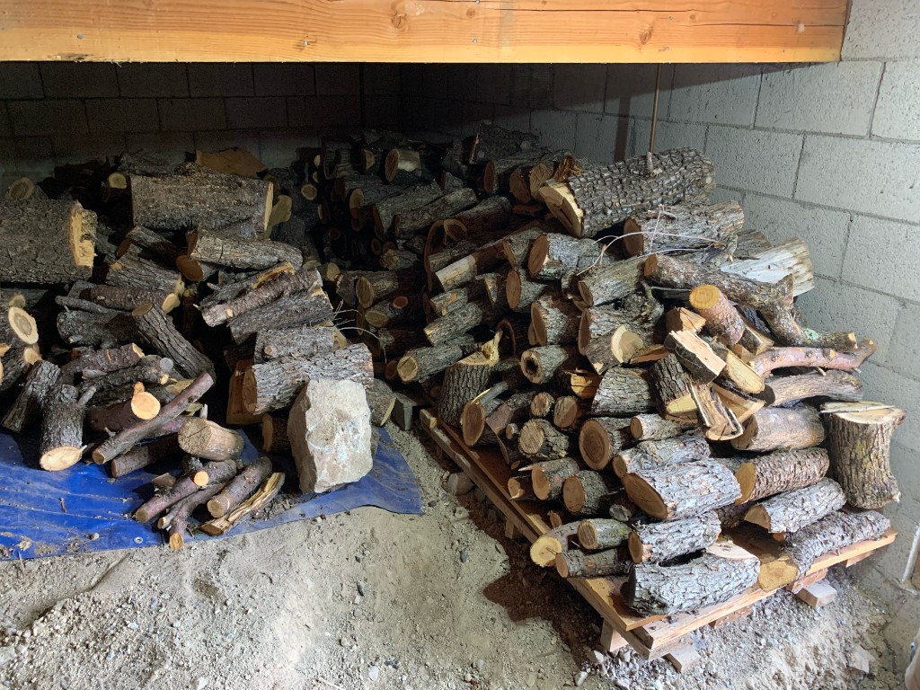 Organized piles of cut logs and branches on a pallet and tarp in a crawlspace